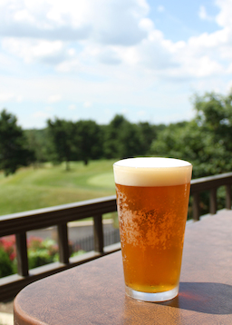 Golden brown beer in frosted glass with golf course in the background.