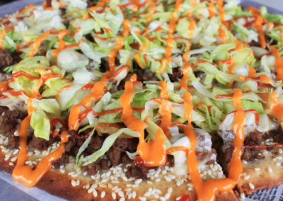 Cheeseburger Pizza on sesame seed crust with ground beef and melted cheese topped with shredded lettuce, ketchup, mayonnaise and thousand island dressing.