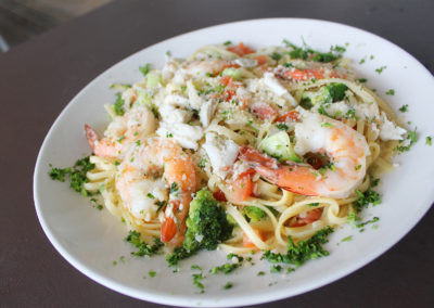 Linguini pasta in white wine sauce with broccoli, lump crab meat pieces, and large shrimp garnished with parsley in a white bowl.